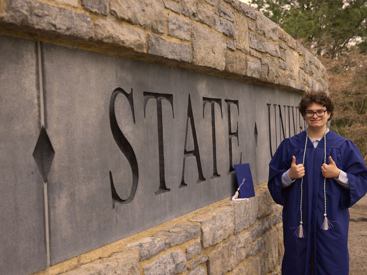 Graduate beside the carved Pennsylvania State University entrance sign