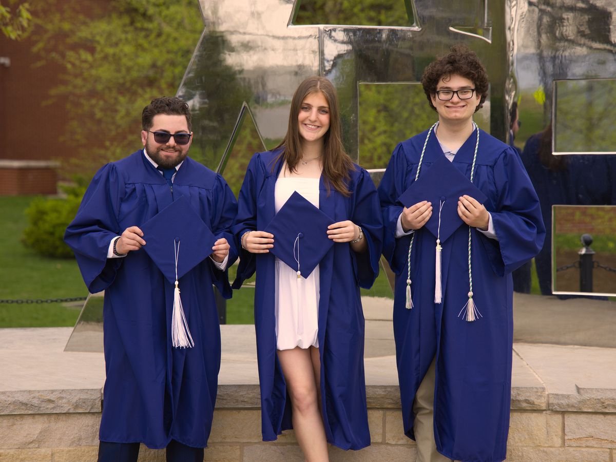 Three graduates in front of the We Are sculpture